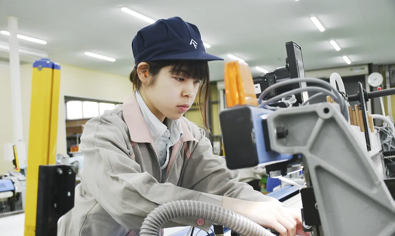 作業服と帽子を着用した女性社員が、機械の操作に集中している。